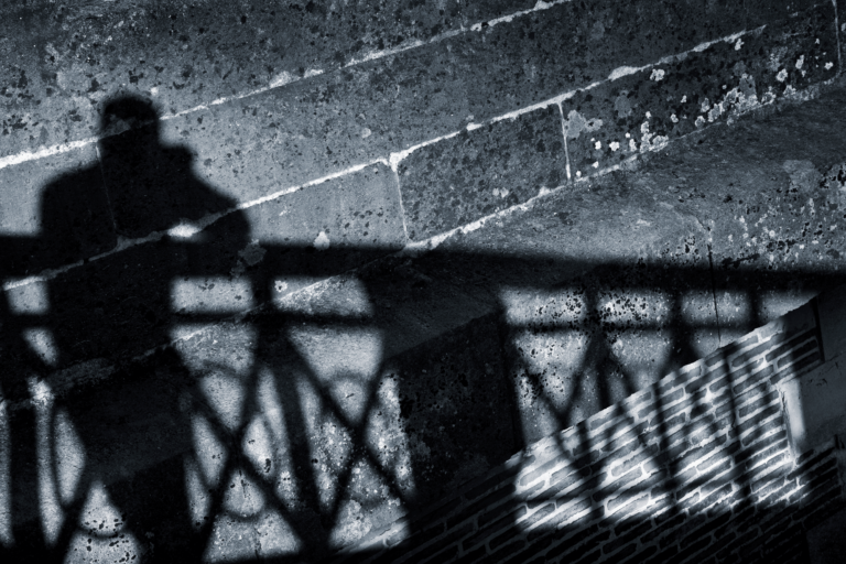 Sombra de hombre apoyado en la barandilla de un puente.